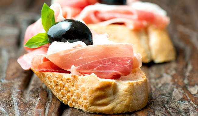 Proscuitto on a small piece of bread with a black olive as a garnish