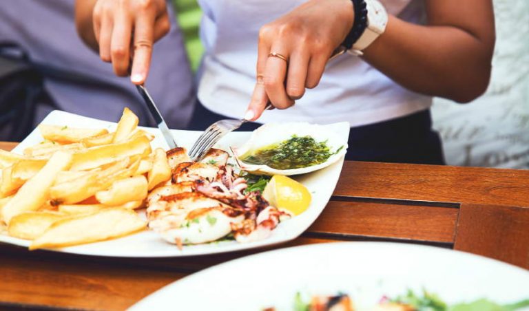 Woman eating a sea food dish with baked potatoes aside