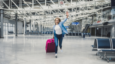 Smiling traveler walking through an airport terminal with a suitcase, suggesting arrival and easy airport pickup transfer.